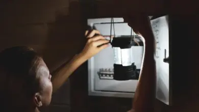 Muž drží svítilnu uvnitř otevřeného elektrického rozvaděče.