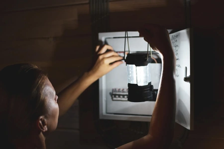 Muž drží svítilnu uvnitř otevřeného elektrického rozvaděče.