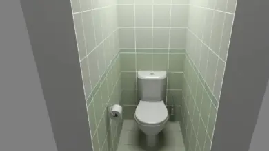 Bílá toaleta v úzké zeleně obložené koupelnové kabince.