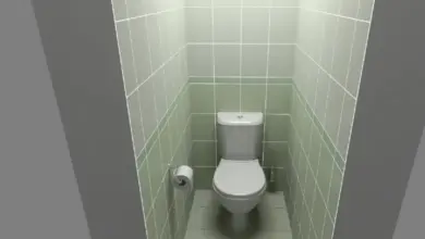 Malá toaletní kabinka s bílým záchodem v zeleně obložené místnosti.