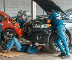 Mechanici opravují černé auto v dílně s otevřenou motorkou.