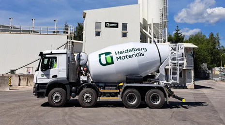 Bílý betonový smíchávač značky Heidelberg Materials před továrnou.