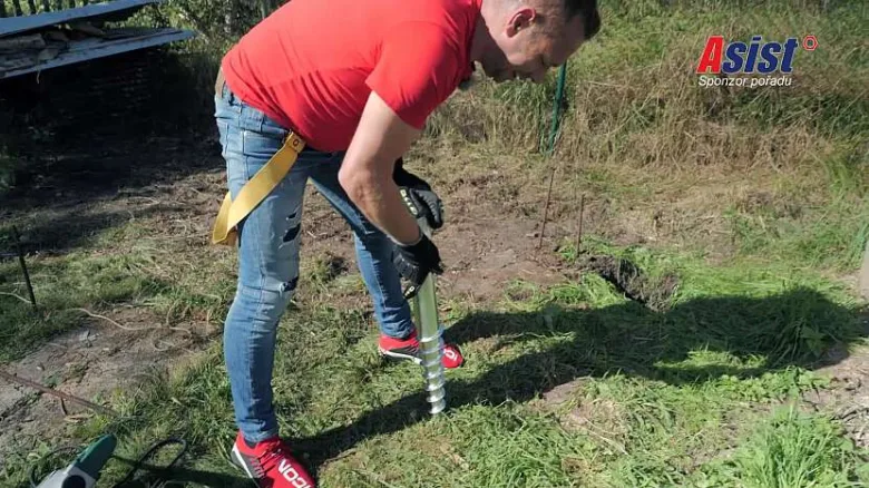 Muž ručně vrtá otvor pro plotový sloup do země.