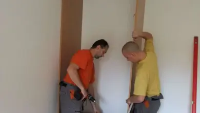 Dva muži montují vestavěnou skříň v prázdné místnosti.