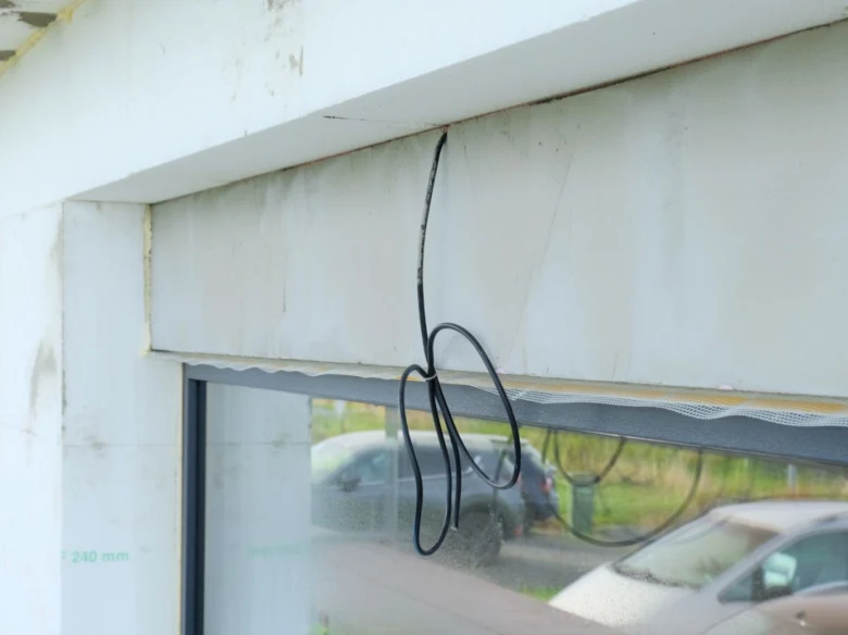 Černý kabel pro venkovní žaluzii visí na okenním rámu.
