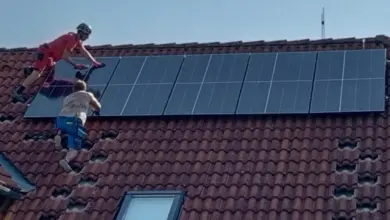 Dva dělníci montují fotovoltaické panely na střechu domu.