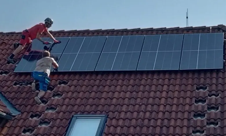 Dva dělníci montují fotovoltaické panely na střechu domu.