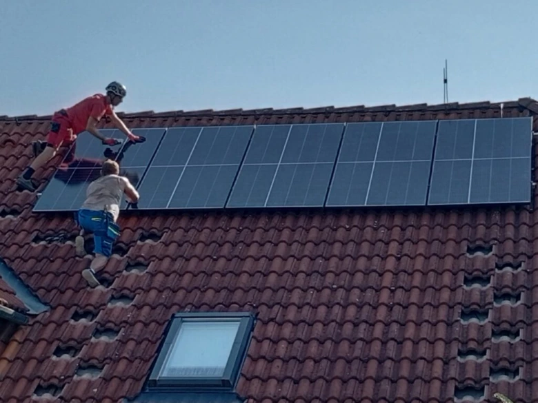 Dva dělníci montují fotovoltaické panely na střechu domu.