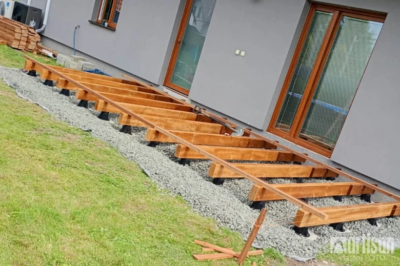 Dřevěné trámy na plastových pilotech pro stavbu terasy.