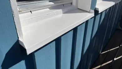 Bílý dřevěný parapet pod oknem na modré fasádě.