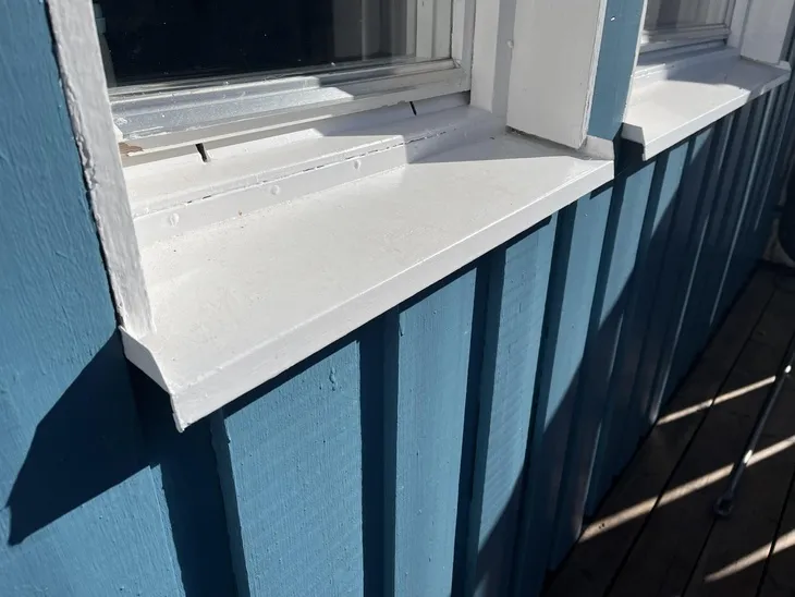 Bílý dřevěný parapet pod oknem na modré fasádě.