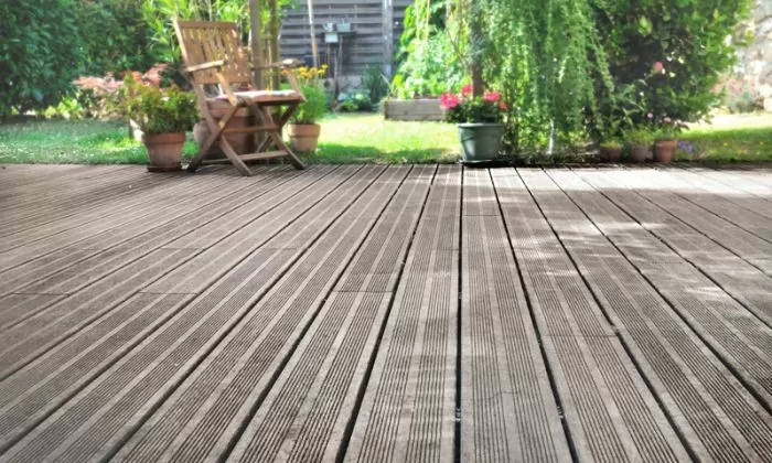 Dřevěná terasa s zahradním nábytkem a kvetoucími rostlinami.