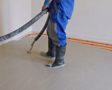 Pracovník nanáší podlahovou maltu v interiéru s topením.