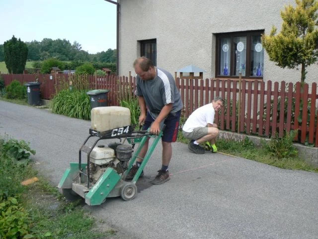 Muži pracují na zpevnění dvora pomocí vibrační desky.