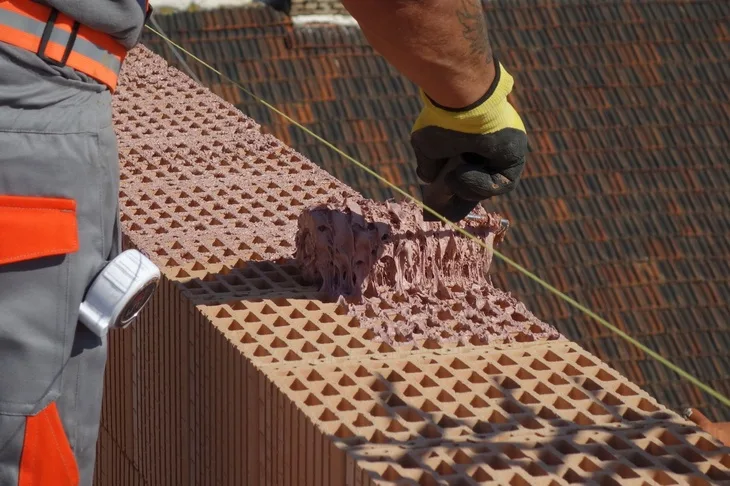 Stavebník nanáší maltu na cihlovou zeď při práci za chladného počasí.