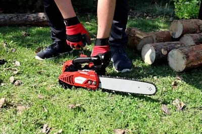 Člověk s řetězovou pilou připravuje křovinořez na trávníku.