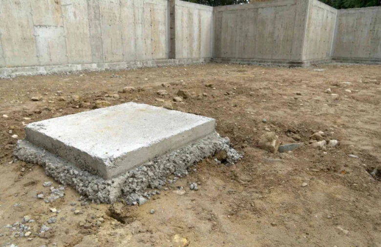 Čerstvě nalitý betonový patník pro dřevostavbu na štěrkovém podkladu.