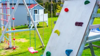 Dřevěné dětské hřiště s lezeckou stěnou a houpačkami na trávníku.