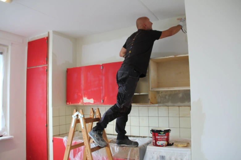 Muž opravuje červené dveře kuchyňské skříně na schodišti.