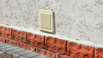 Žlutý větrací otvor na zdi garáže nad červenými cihlami.