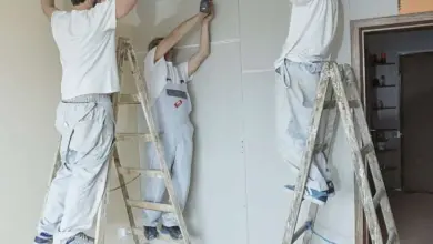Tři muži montují sádrokartonový strop na lešení.