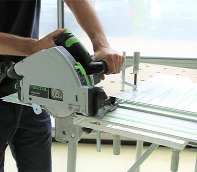 Muž řezá plexisklo pilou na kolejnici značky Festool.