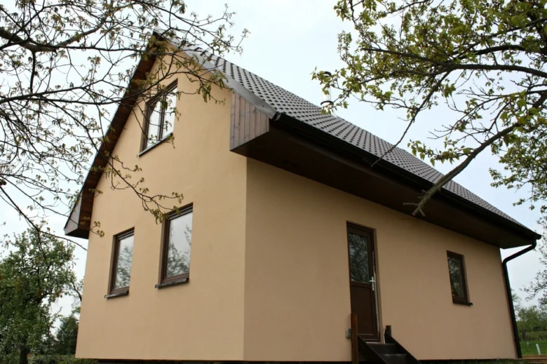 Malý dům s tmavou střechou obklopený stromy.