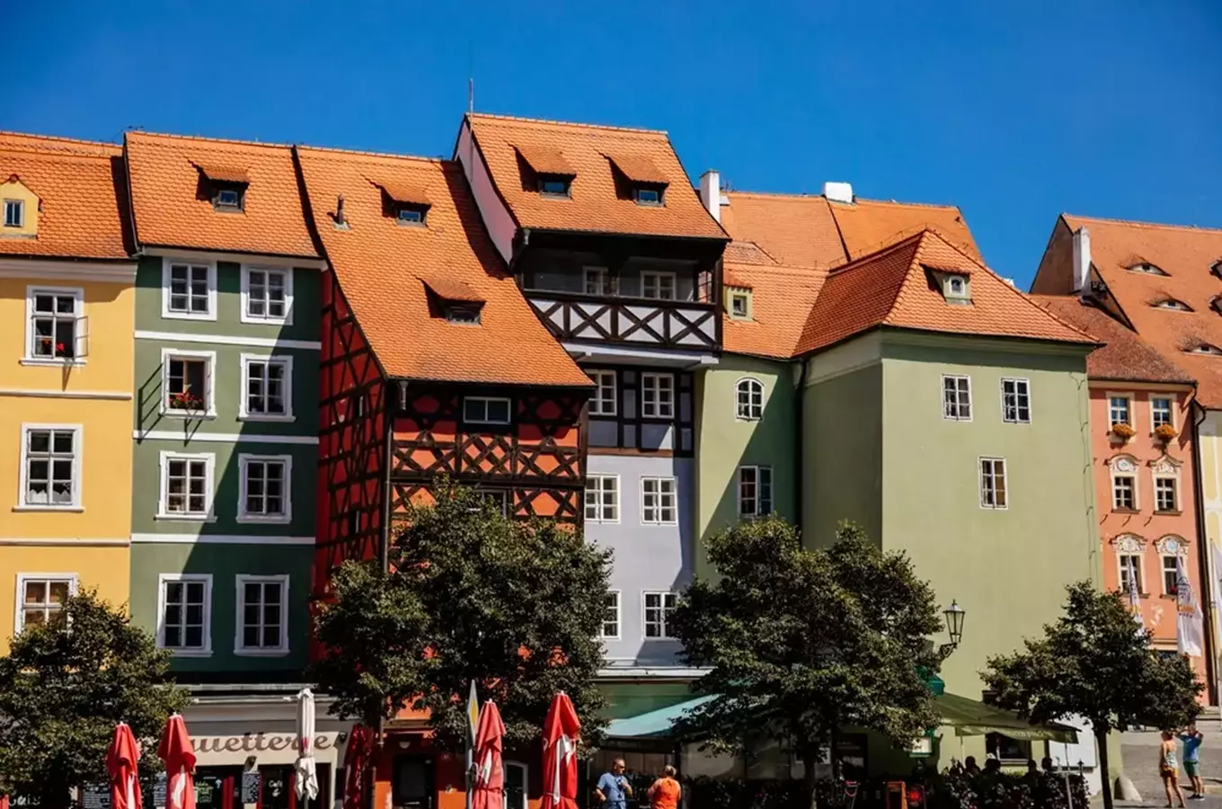 Řada barevných hrázděných domů s půdorysnými střechami.