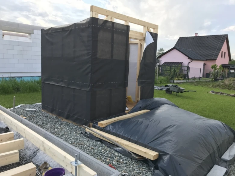 Stavba venkovní sauny z dřeva s černou plachtou na štěrkovém podkladu.