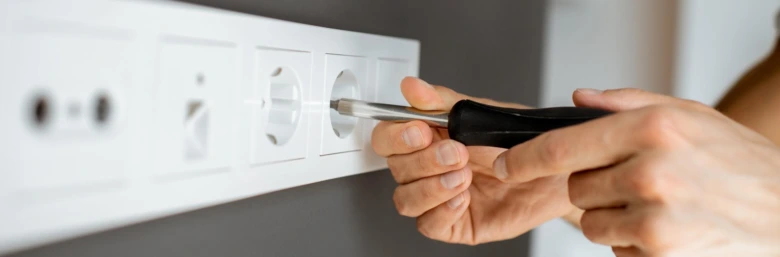 Ruční montáž elektrické zásuvky do zdi šroubovákem.