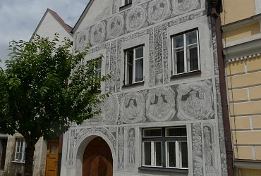 Historická budova se psaníčkovým sgrafitem a erbami na fasádě.