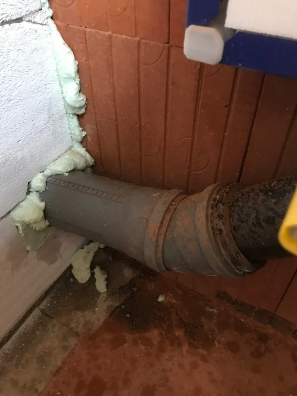 Přesný detail zateplení potrubí pěnou u stěny při instalaci Geberitu.