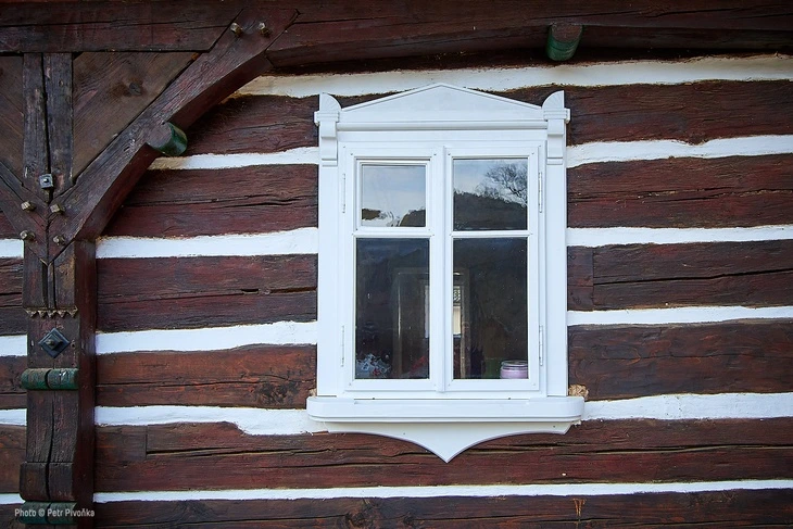 Detail bílého okna v hrázděné stavbě s tmavými dřevěnými trámy.