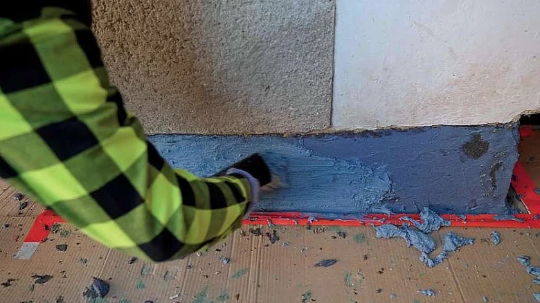Náplast hydroizolace na základnu domu pomocí špachtle.