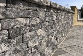 Kamenná opěrná zeď postavená na svahu vedle chodníku.