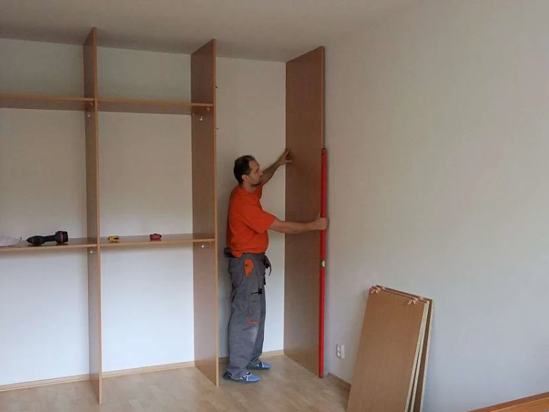 Muž montuje dveře vestavěné skříně v interiéru.