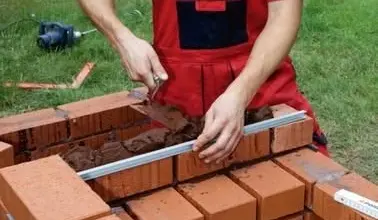 Muž staví cihlový gril na zahradě pomocí úrovně.