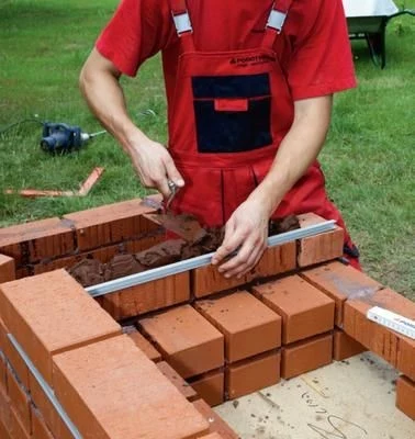Muž staví cihlový gril na zahradě pomocí úrovně.