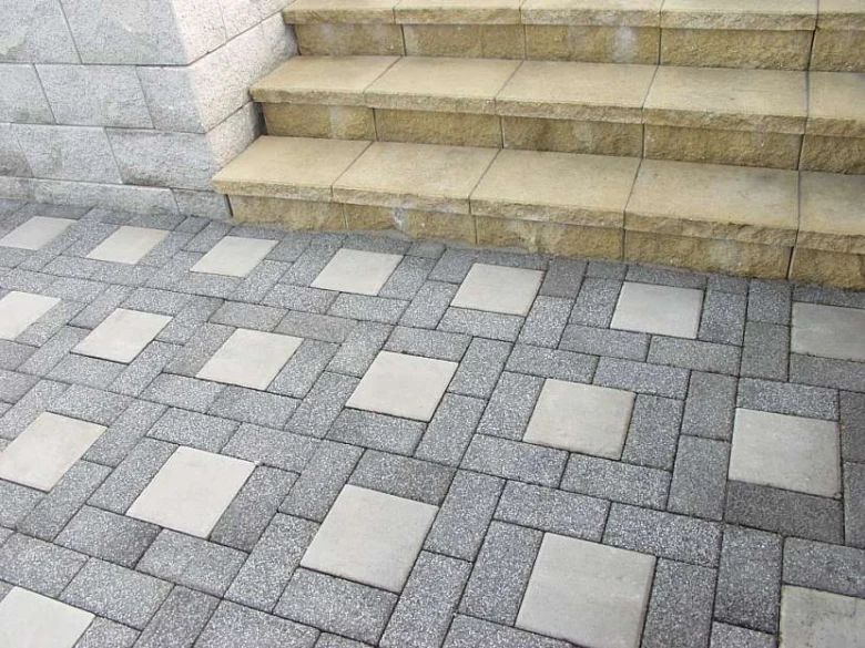 Venkovní schody z šedé zámkové dlažby s kamenným podestem.