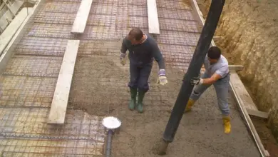 Dva dělníci nalévají beton do základu bazénu s výztuhou.