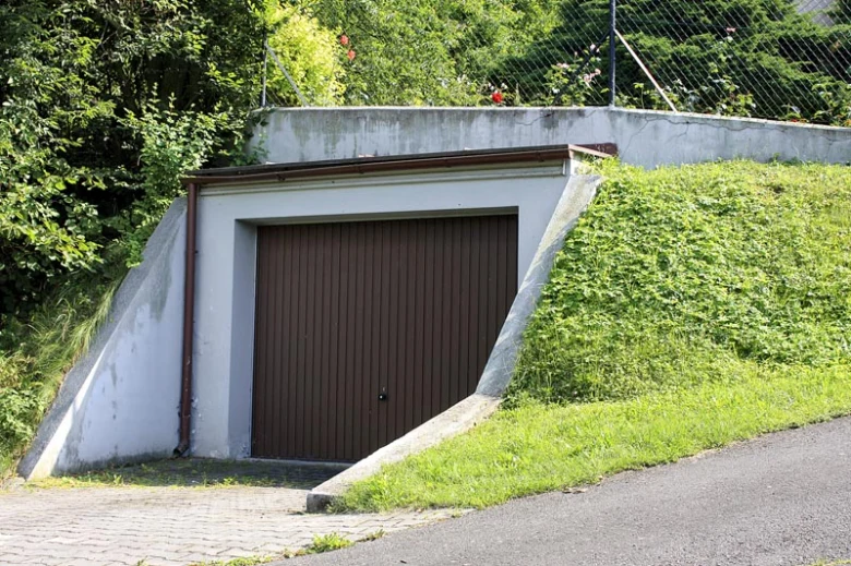 Garáž zapuštěná do svahu s bránou a zeleň