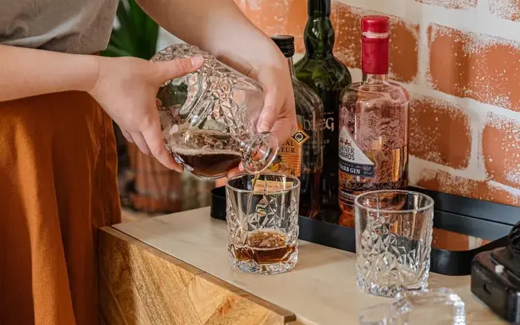 Nalévání whisky do sklenice na dřevěném stole v podkroví.