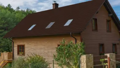Dvoupatrový dům s hnědou dřevěnou fasádou a tmavými taškovými střechami.