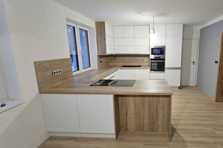 Moderní kuchyň s bílými skříněmi a dřevěnou pracovní deskou.