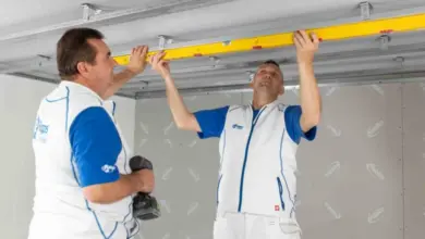 Dva muži montují sádrokarton na dřevěný strop pomocí úrovně.