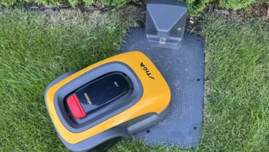 Žlutá robotická sekačka na nabíjecím stanovišti v zahradě.