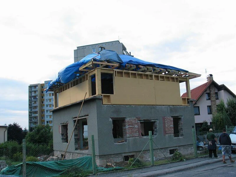 Přístavba k domu s odkrytou konstrukcí a modrou plachtou.