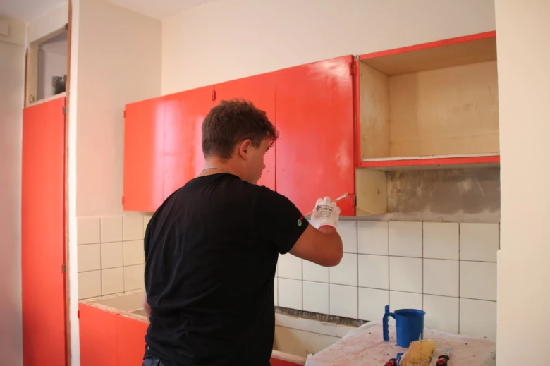 Muž maluje červené kuchyňské skříňové dveře při renovaci.