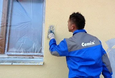 Muž maluje fasádu domu, údržba exteriéru budovy.