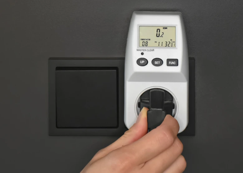 Ruka zasouvá měřič spotřeby do zásuvky pro sledování energie.